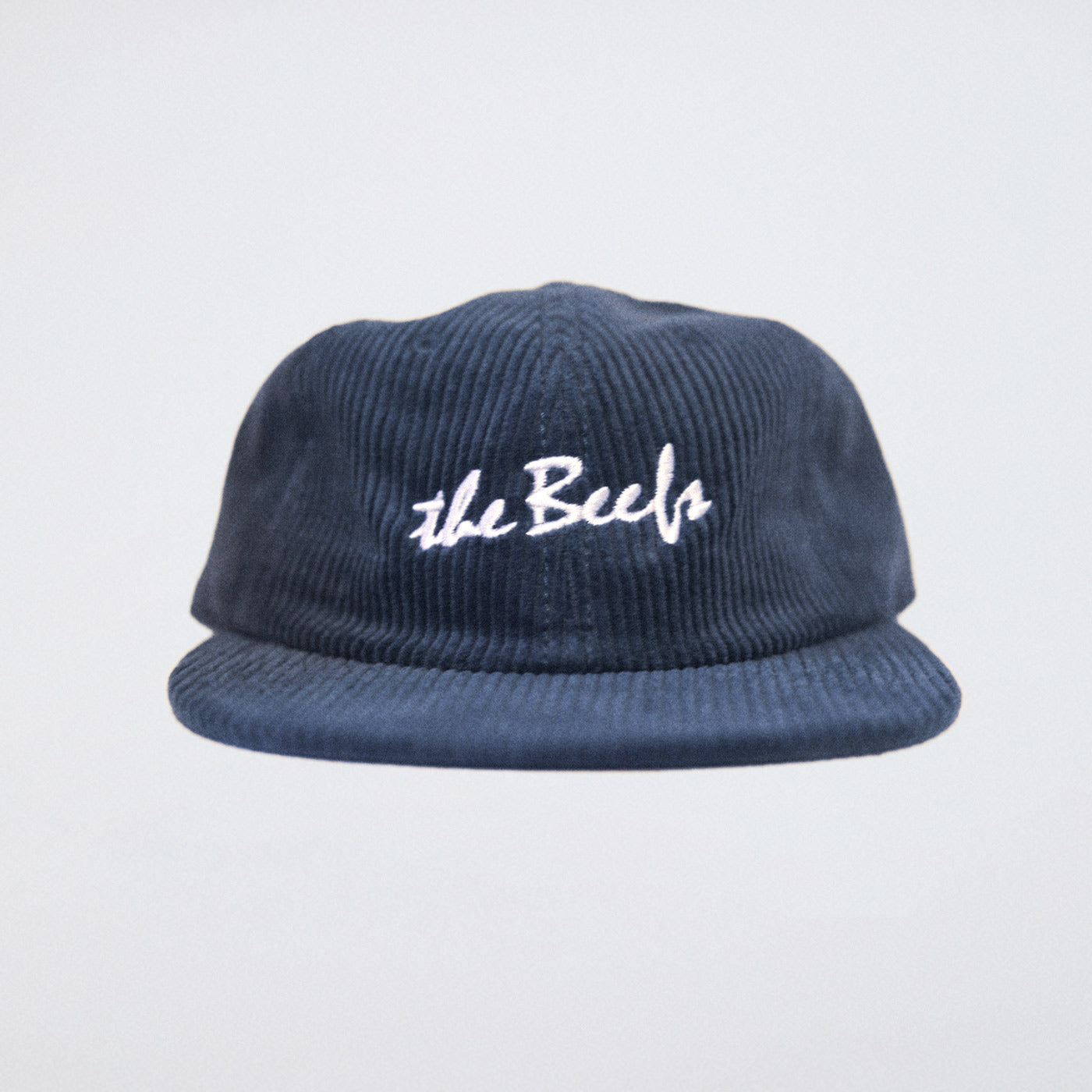 A steel blue cord cap with The Beefs logo photographed in a studio