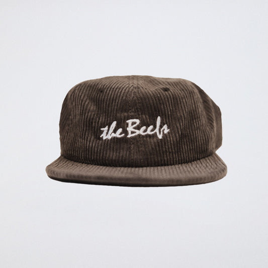 A brown cord hat with The Beefs logo photographed in a studio