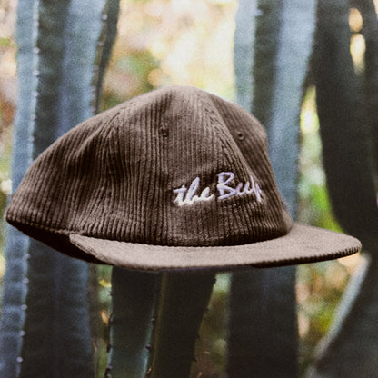 A brown cord hat photographed on an angle hanging on a cactus